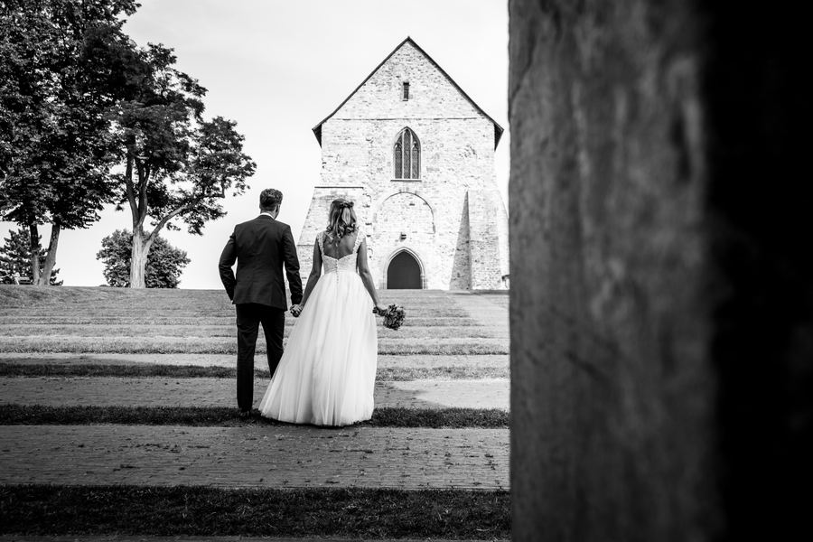 Brautpaar vor einer Kapelle, fotografiert durch einen Torbogen – Schwarz-Weiß-Hochzeitsfoto